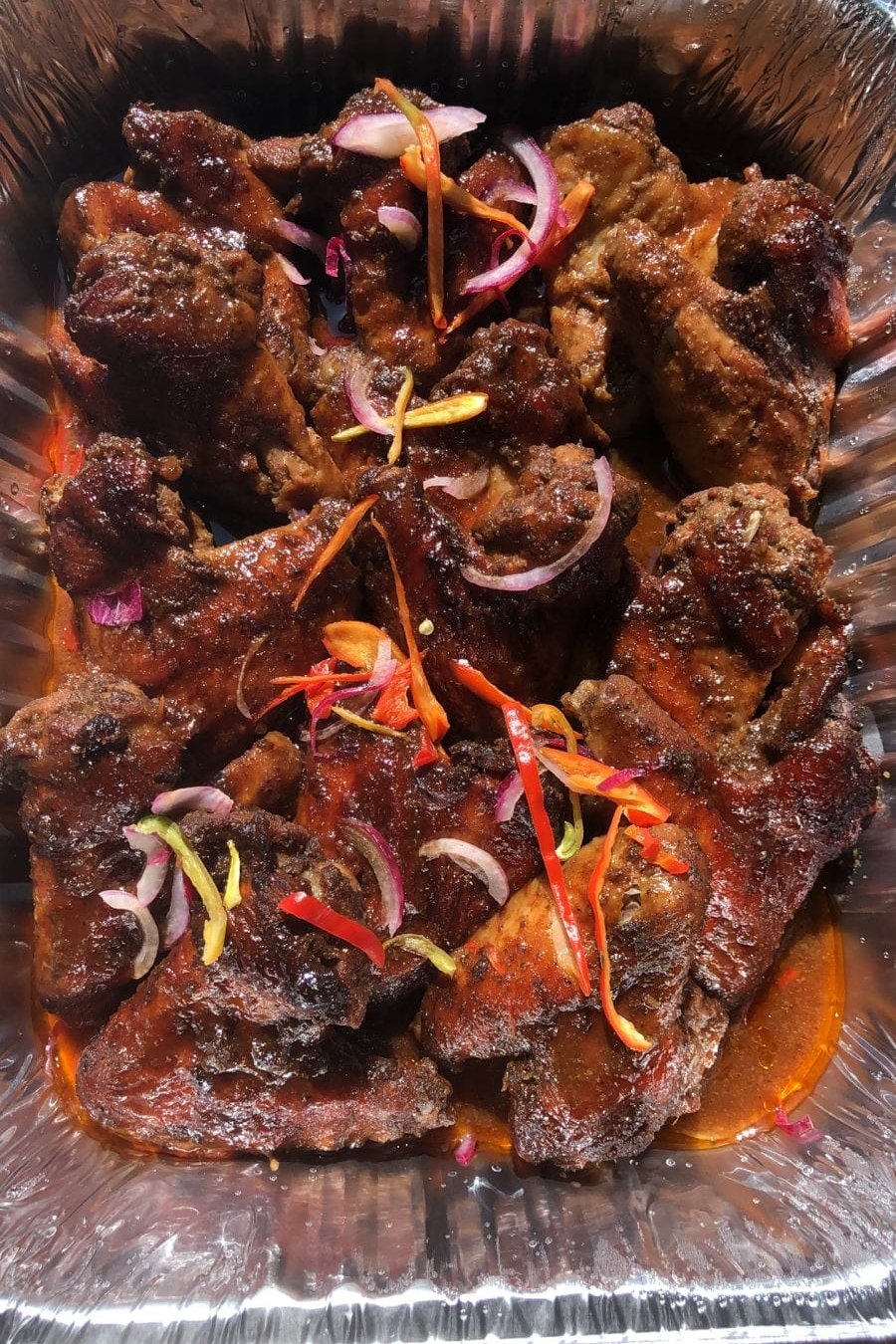 Glazed chicken in a foil tray topped with red onion and peppers